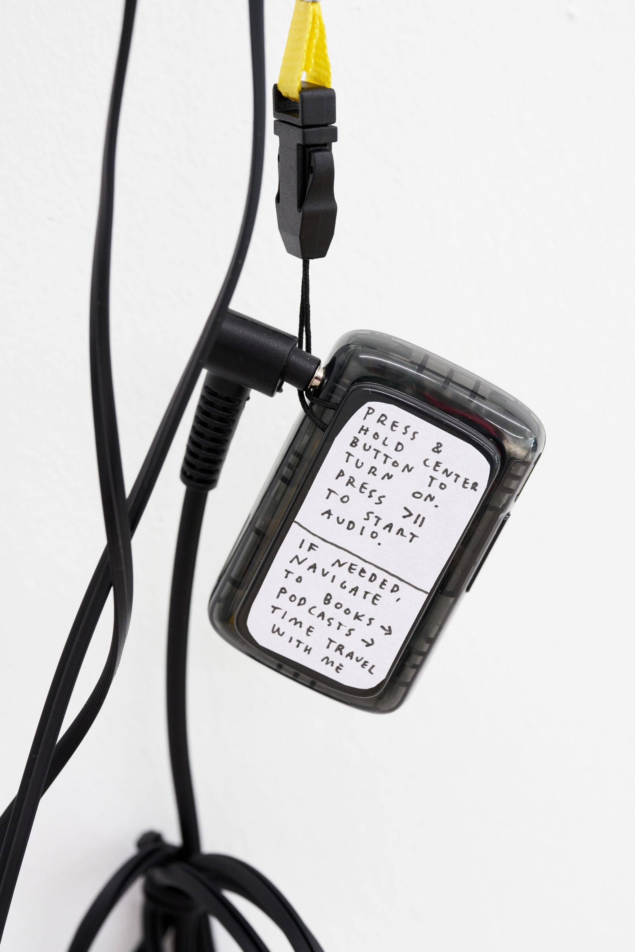 Finnegan Shannon, Time travel with me (detail), 2022, Audio, mp3-Player, lanyard, headphones, transcript, zine, Image description: The back of a mp3 player. On it there’s a sticker with a handwritten instructions for how to play the audio.